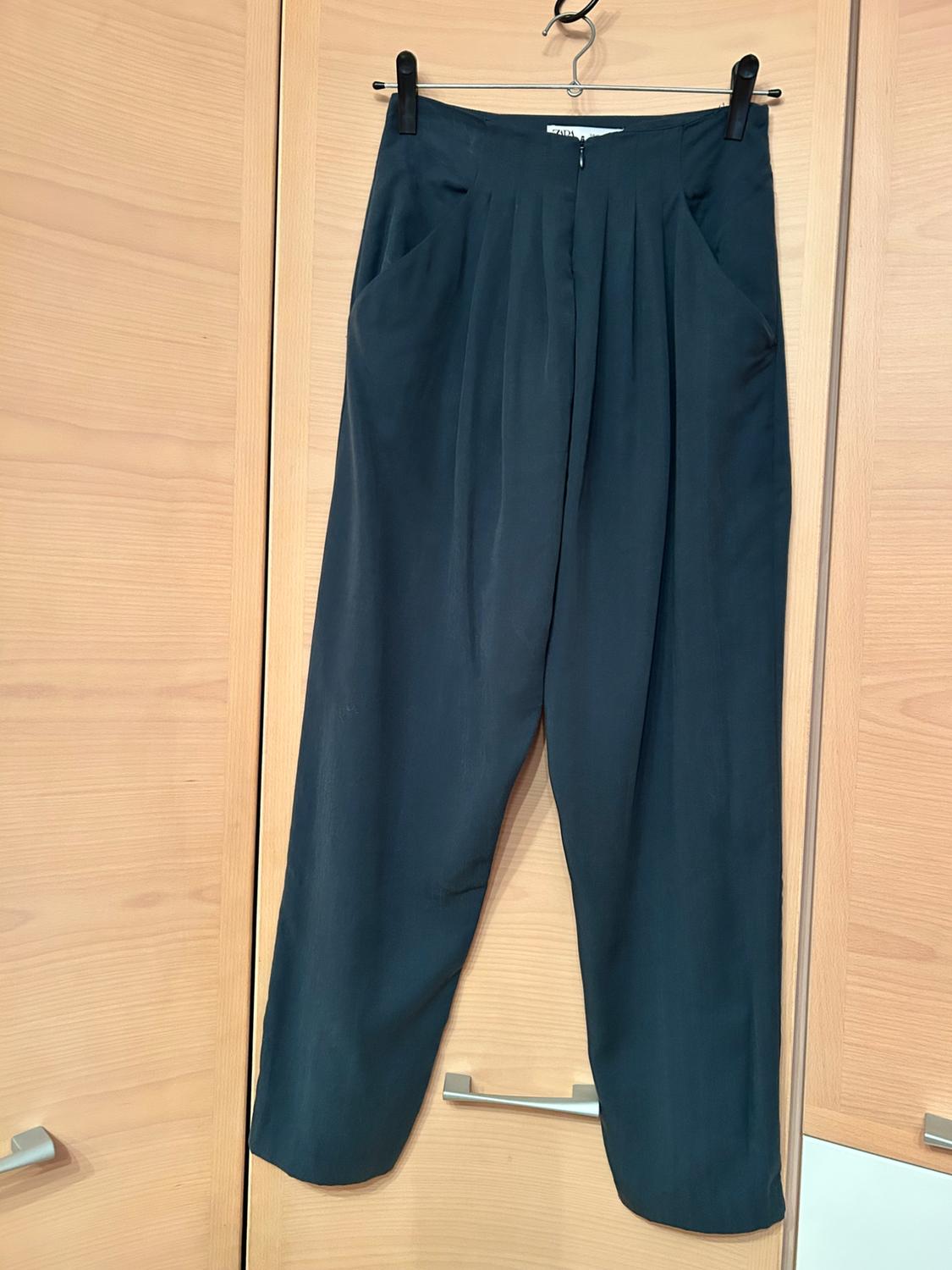 Front view of black trousers with pleats and side pockets.