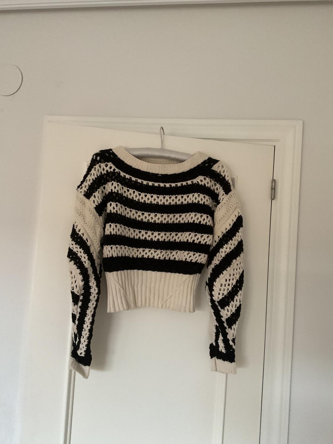 Knitted jumper hanging on a door, with a black and white striped design, long sleeves and a round neck. Indoor setting.