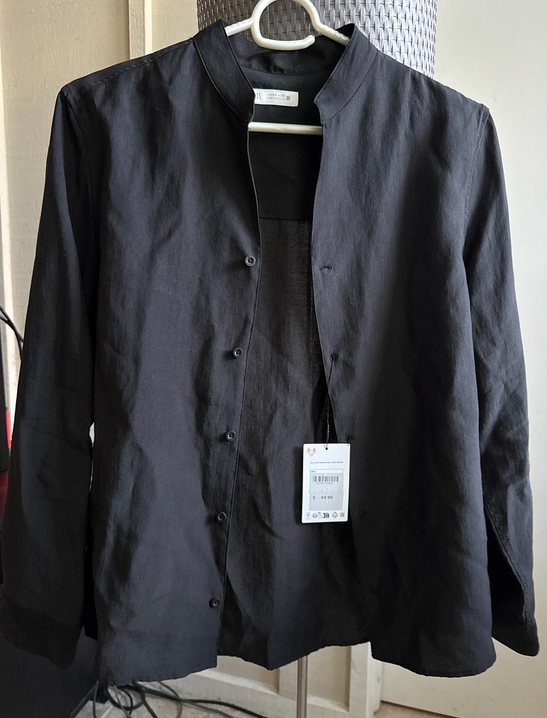 Black long-sleeve shirt with a mandarin collar hanging on a white hanger indoors. It has a visible tag displaying the text “$49.90.”