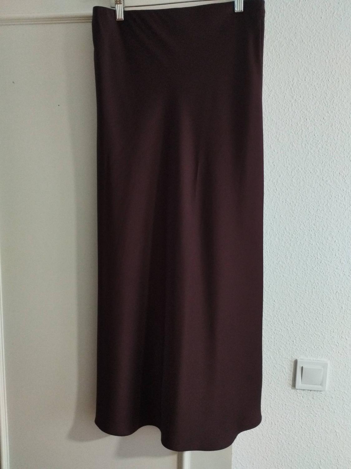 Long brown skirt hanging on a hanger over a white door, with a smooth texture and straight drape. White wall background.