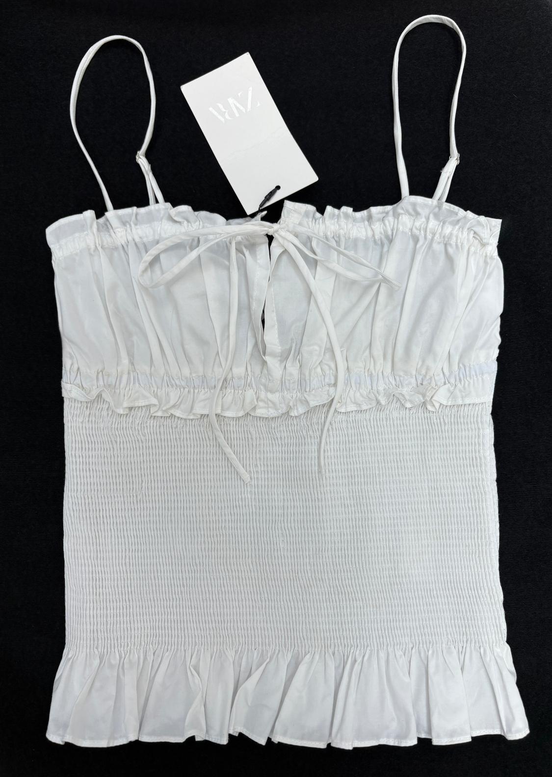 White top with thin straps and ruched detail, on a black background. White label with "RAZ" text hanging from the strap.