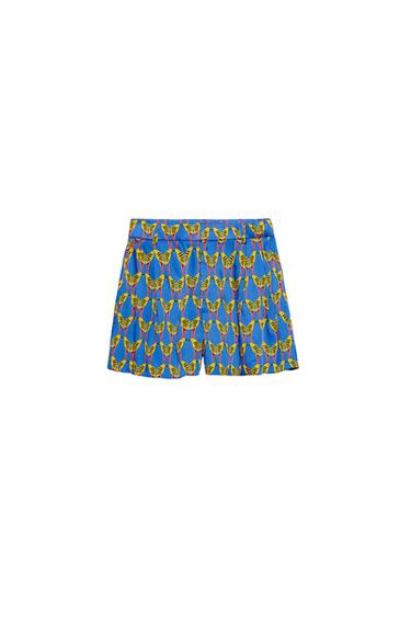 Blue shorts with yellow leaf print and red detailing. White background. Vibrant and colourful design.