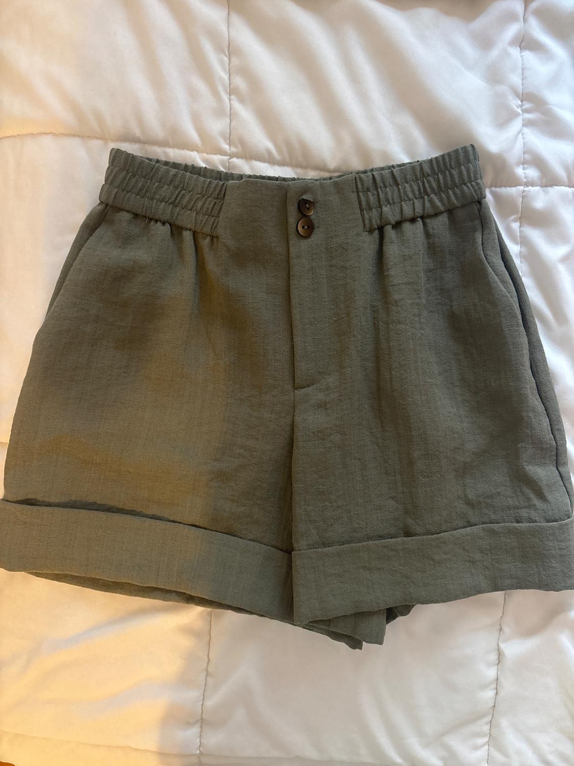 Olive-green shorts with an elasticated waist, two buttons and turn-ups, on a white sheet.