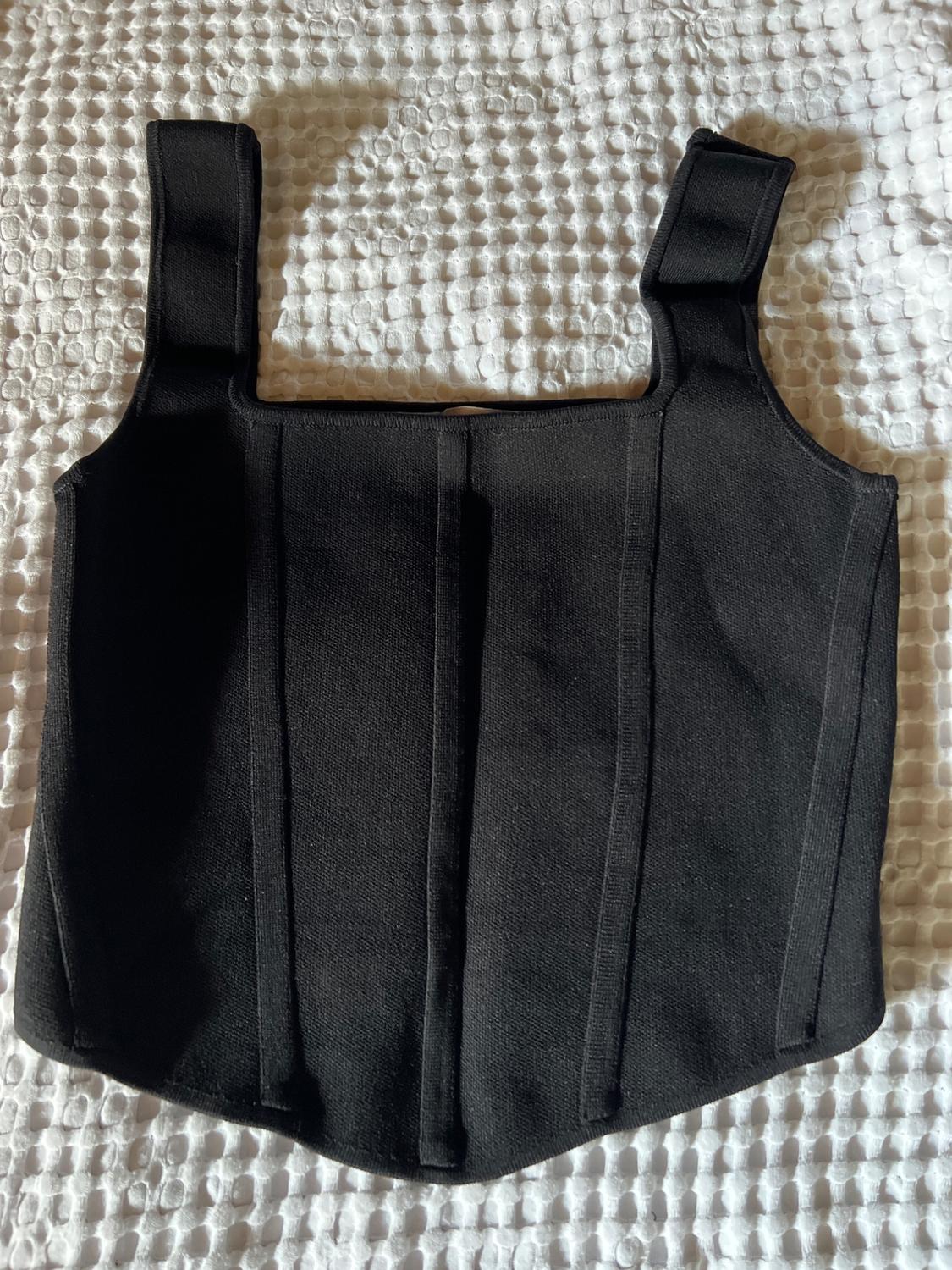 Black top with wide straps and vertical seams, on a white textured blanket in a relaxed composition.