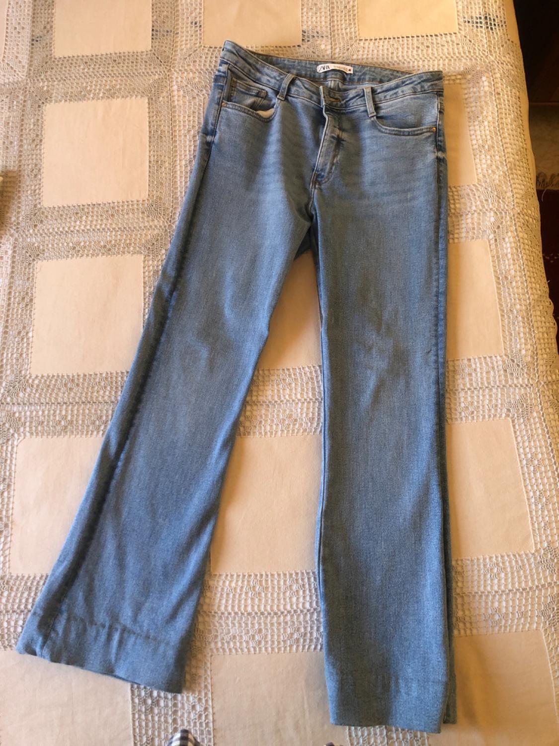 Blue wide-leg jeans on a beige checked bedspread. Label visible on the waistband.