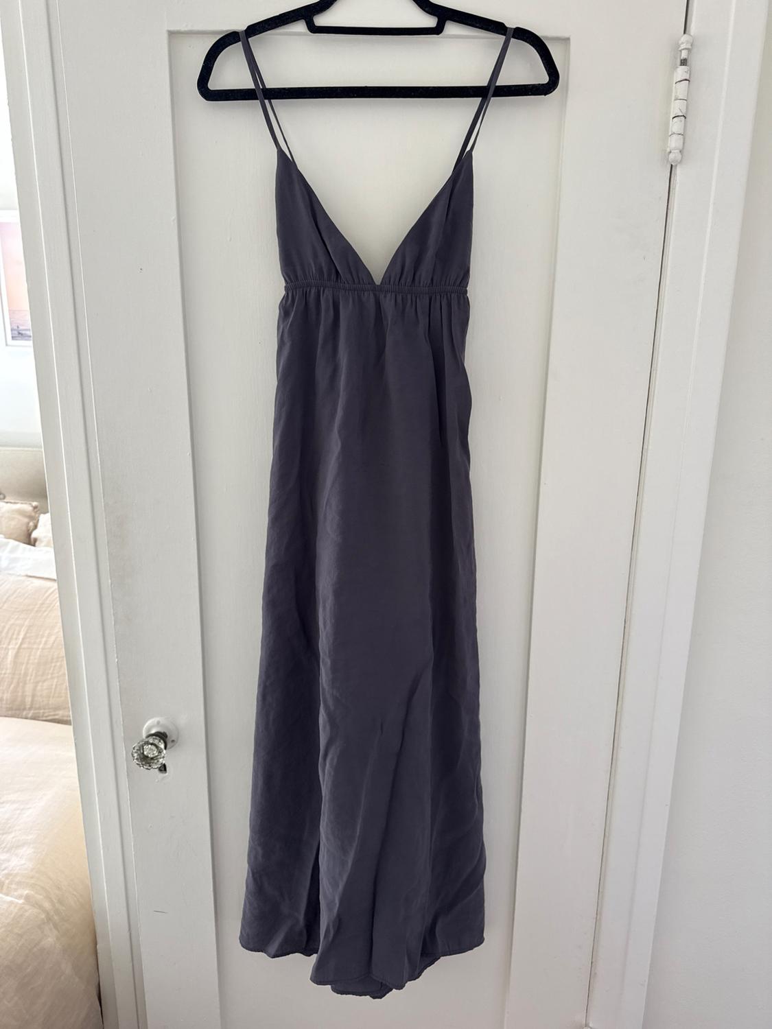Gray long dress with thin straps and V-neckline, hanging on a black hanger over a white door.