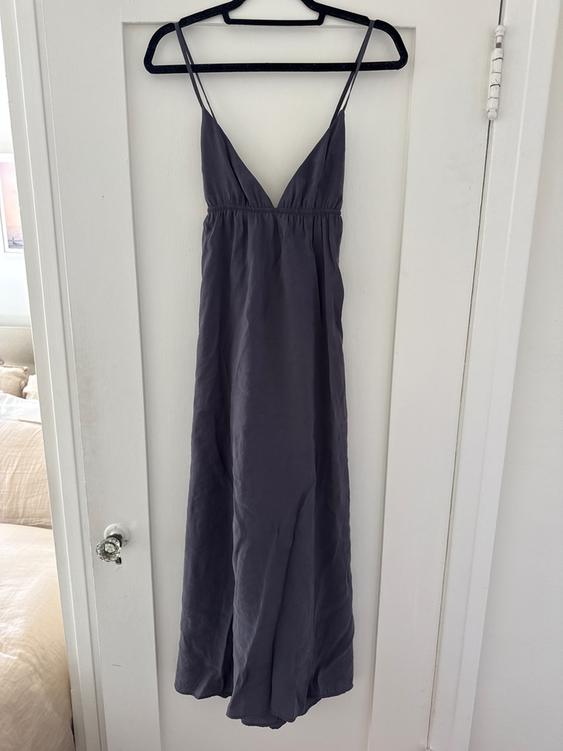 Gray long dress with thin straps and V-neckline, hanging on a black hanger over a white door.