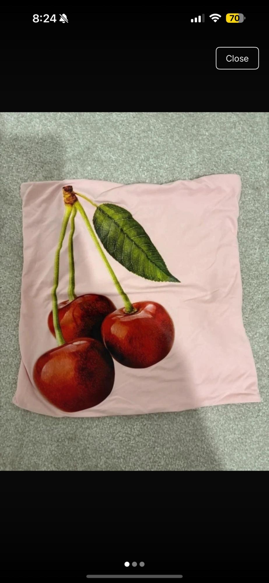 Light pink garment with a pattern of three red cherries and a green leaf on a grey carpet. Text: 8:24, 70, Close.