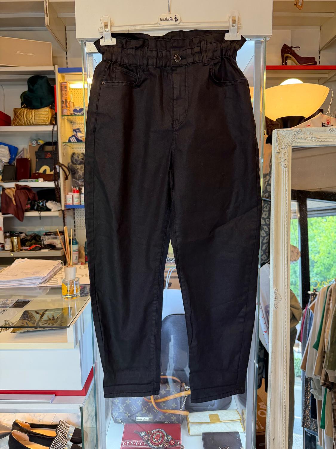 Black trousers hanging on a white hanger in a shop. Background with shelves full of accessories and clothes.