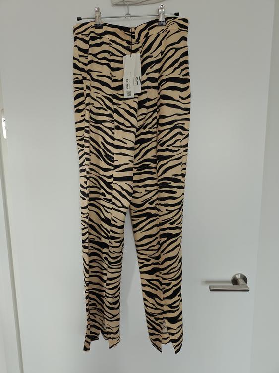 Zebra print trousers in beige and black tones hanging on a hanger. Visible label with text: "Urban Life".