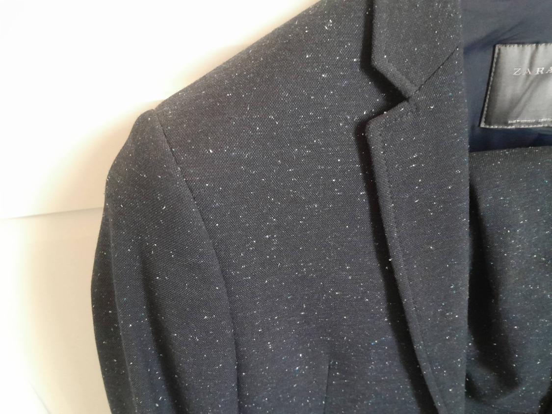 Black jacket with a white flecked texture, hanging on a hanger. Visible label with the brand "ZARA" on the inside.