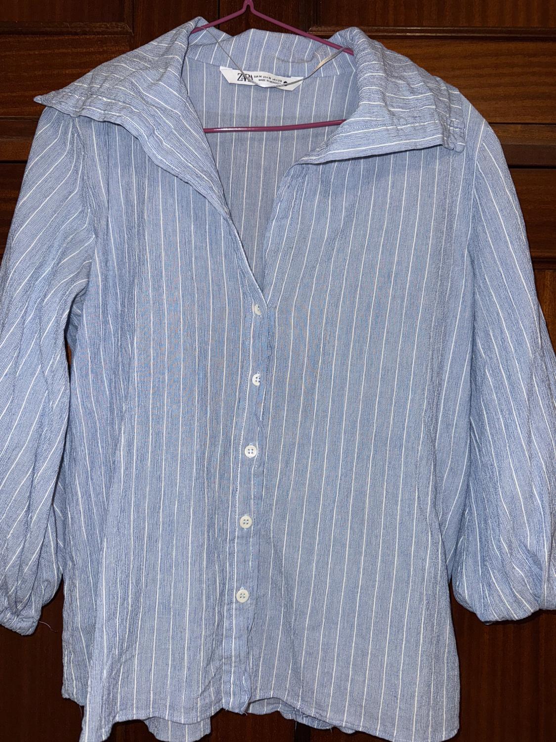 Blue and white vertical striped shirt hanging on a pink hanger. Brown wooden background. Visible label on the collar.