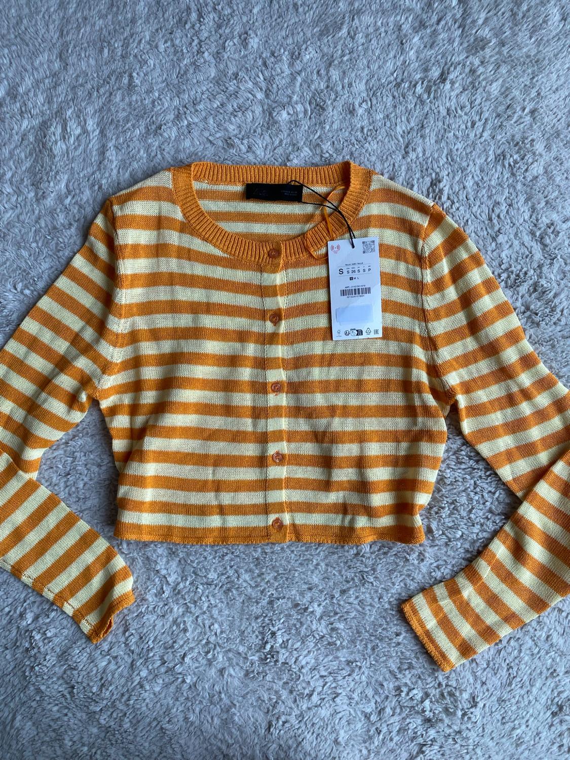 Orange and yellow horizontal stripe knit cardigan, long sleeves and front buttons, on a fluffy white rug.