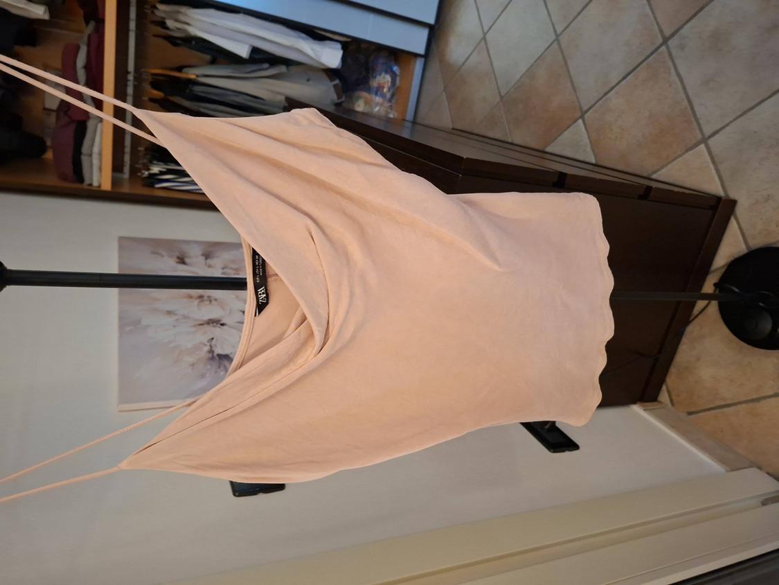 Light pink strappy top hanging on a black clothes rail, with an open wardrobe and tiled floor in the background.