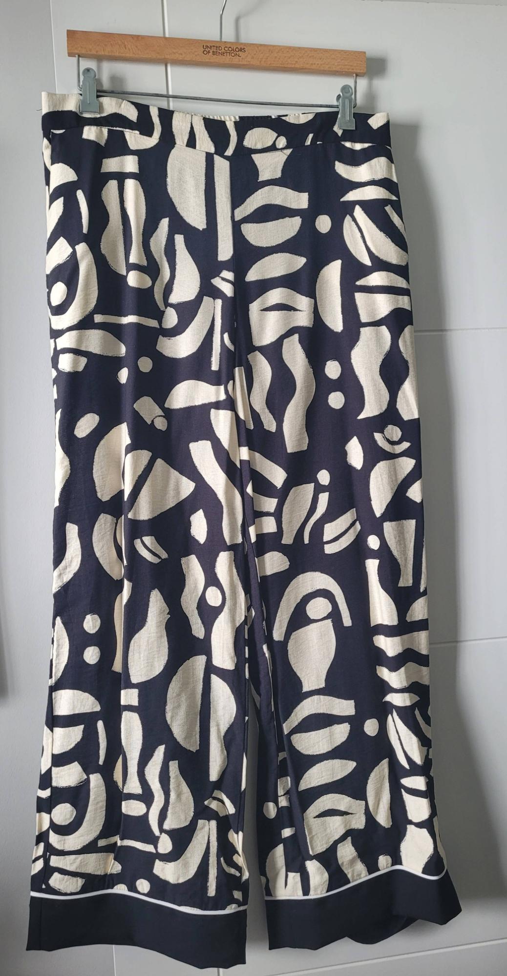 Trousers hanging on a wooden hanger with a black and white abstract pattern. Visible text: "United Colors of Benetton".