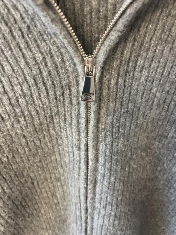Metal zipper closure on a chunky ribbed gray sweater, close-up.