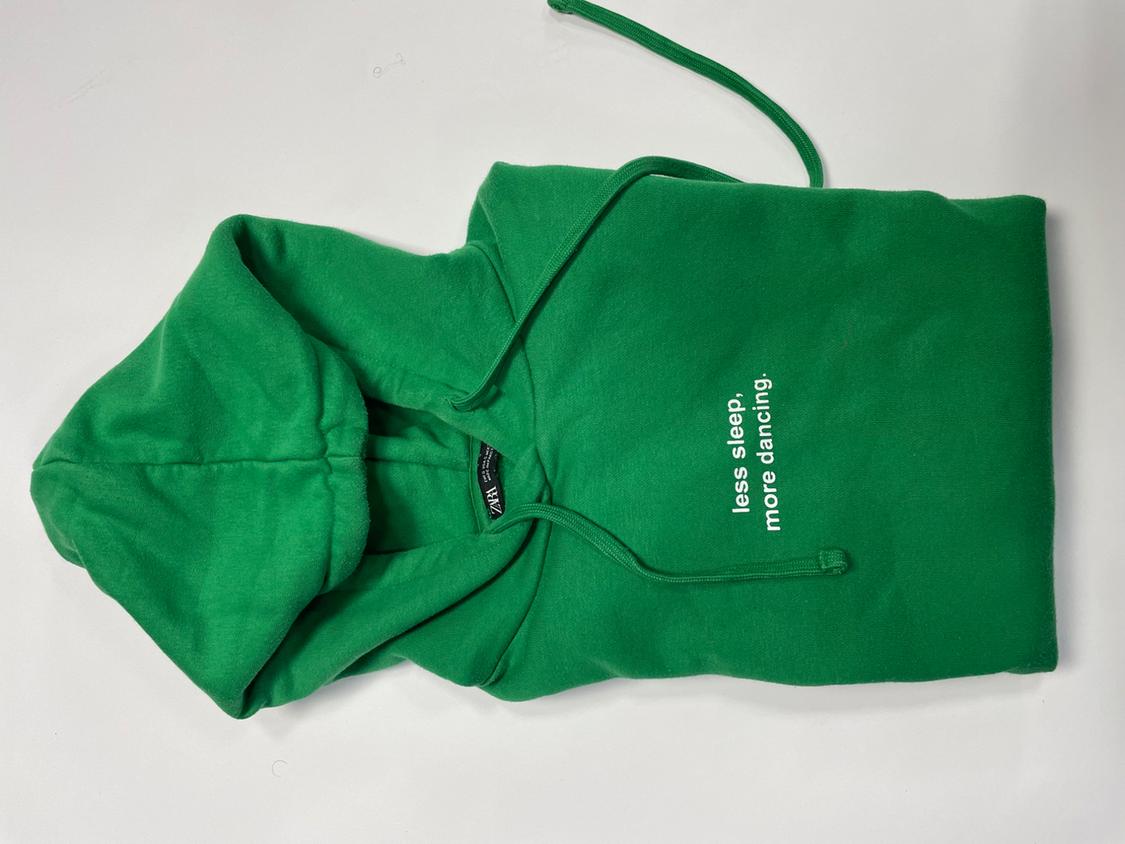 Green hooded sweatshirt folded on a white background. Text: less sleep, more dancing.