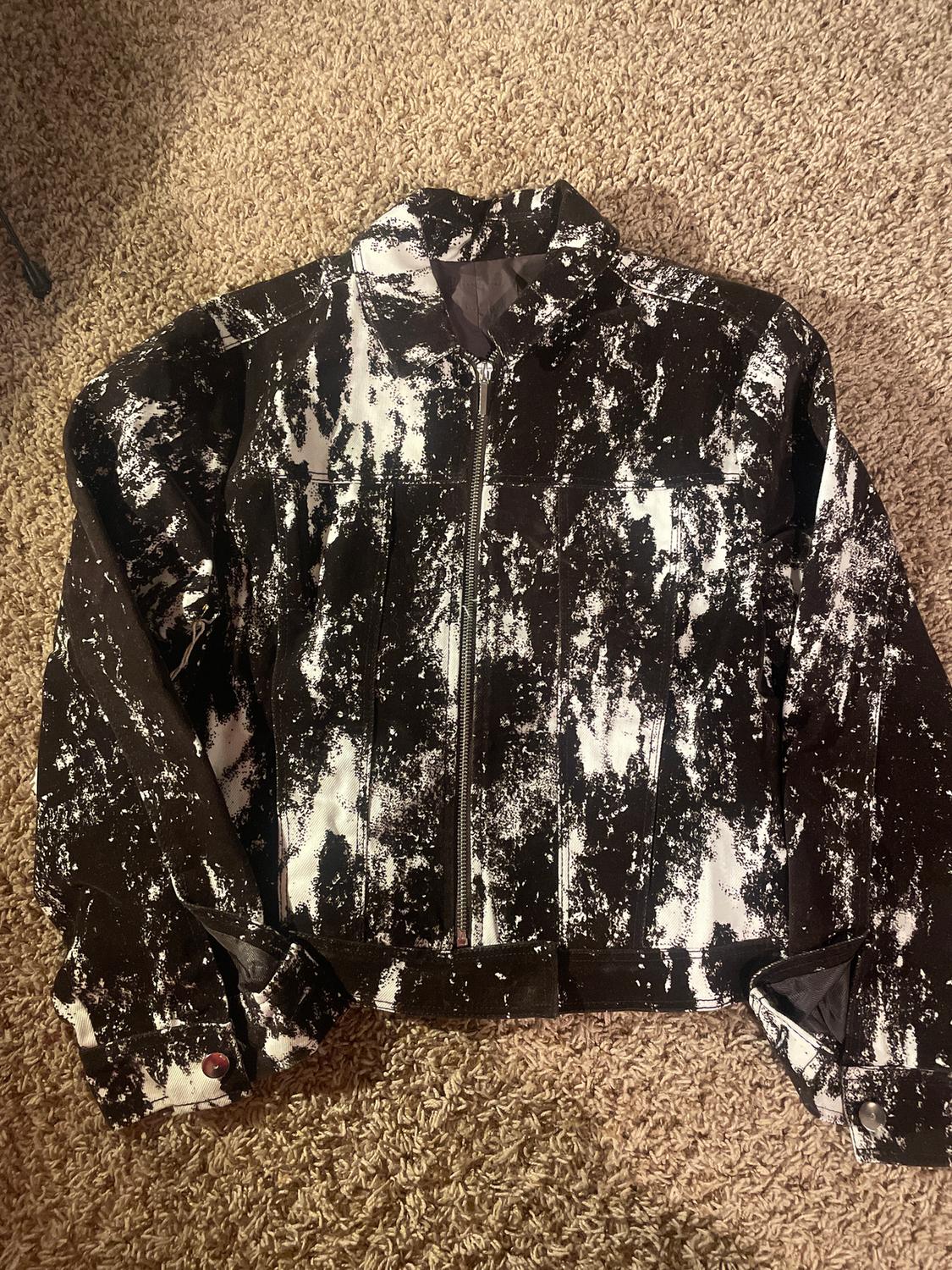 Black jacket with an abstract white print, front fastening and buttons on the sleeves, on a beige rug.