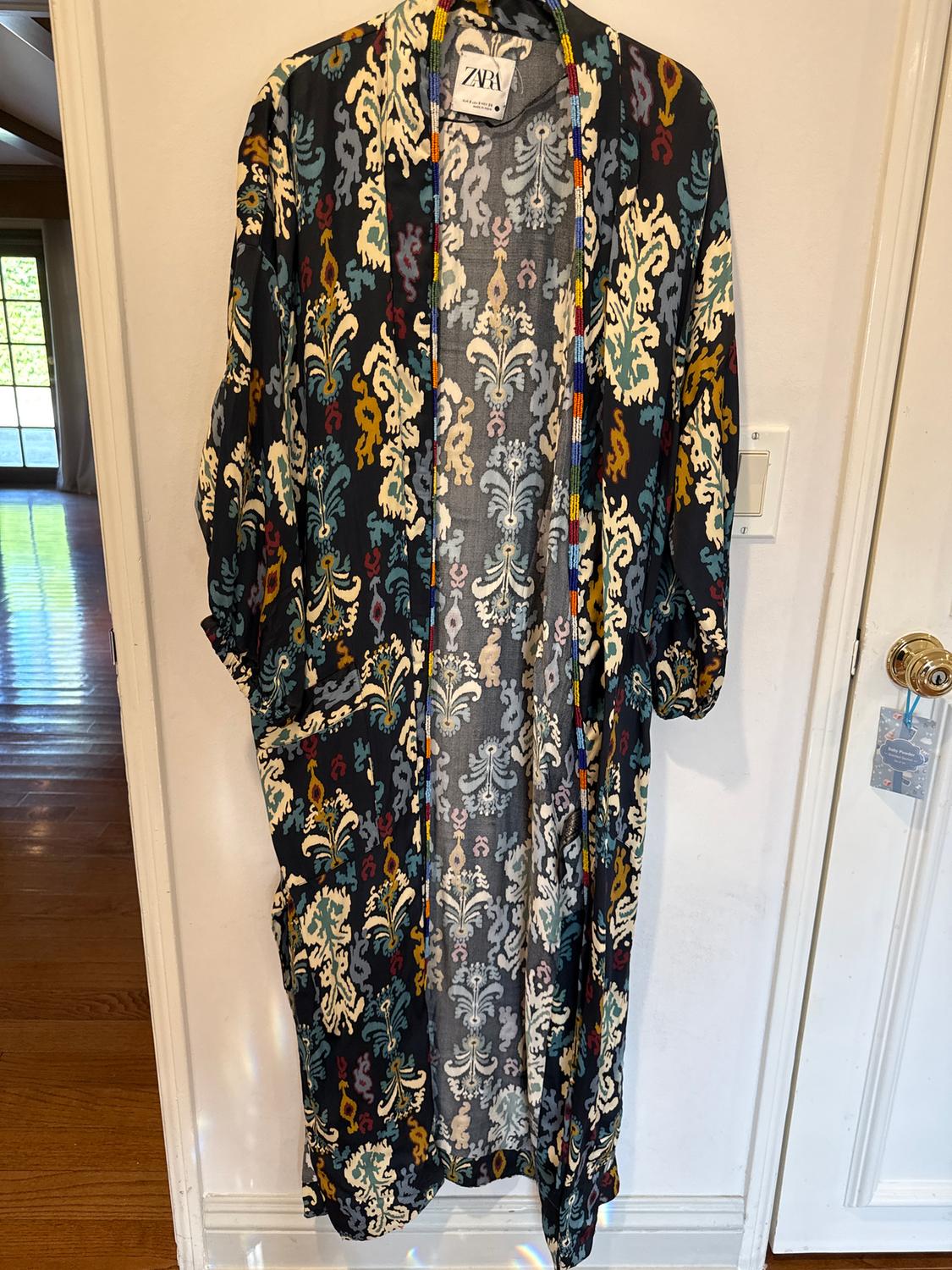 Kimono hanging with a floral print in blue, white, and yellow tones. Visible "ZARA" tag. White door in the background.