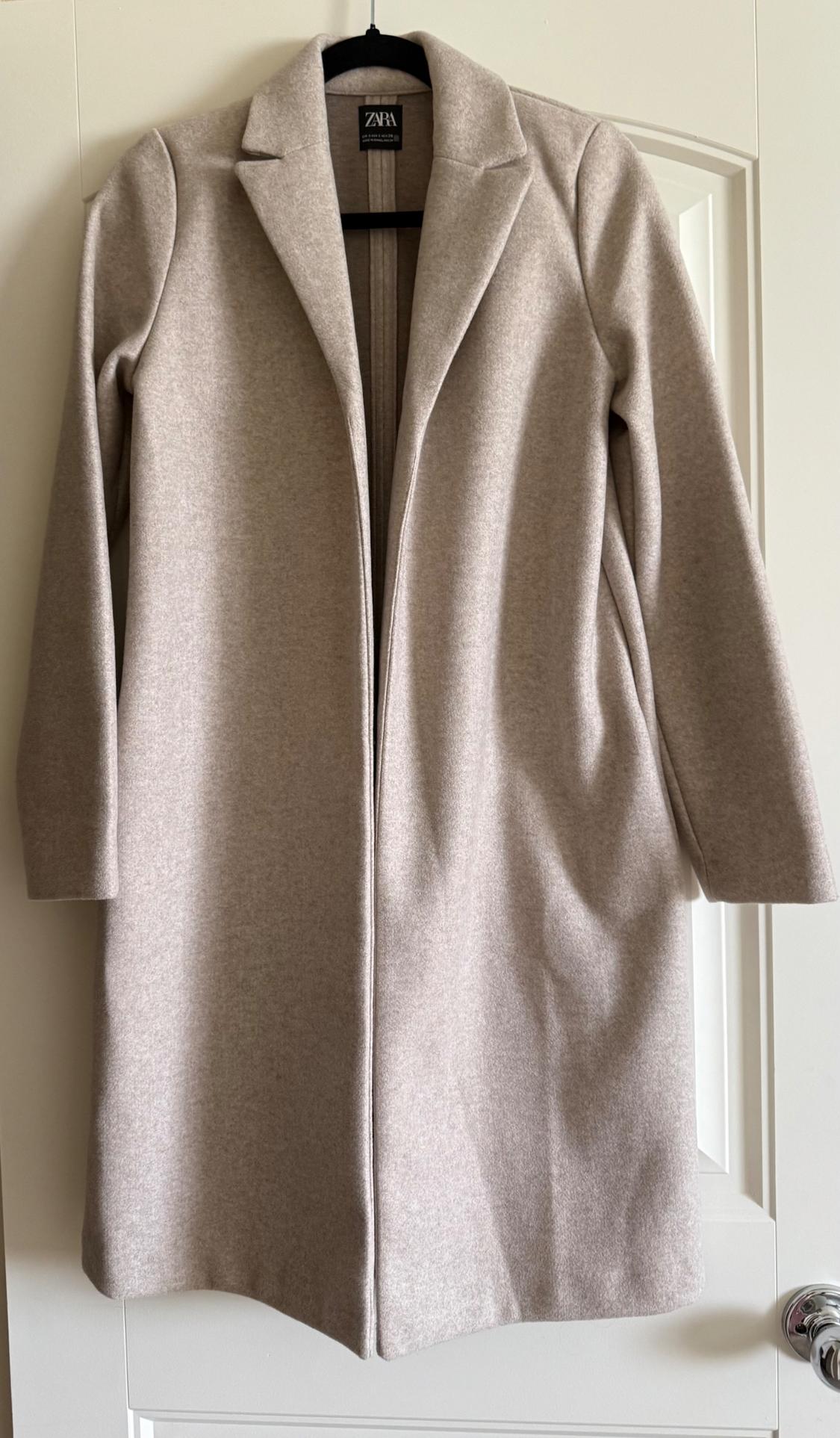 Front view of a long beige coat with lapels and long sleeves.