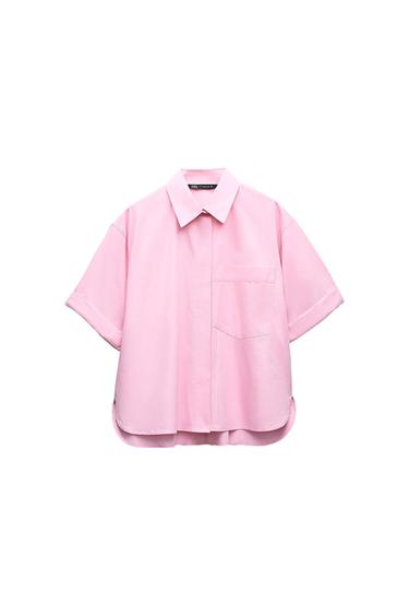 Short-sleeved light pink shirt with collar, front pocket and asymmetric hem on a white background. Interior label with the text ZARA.