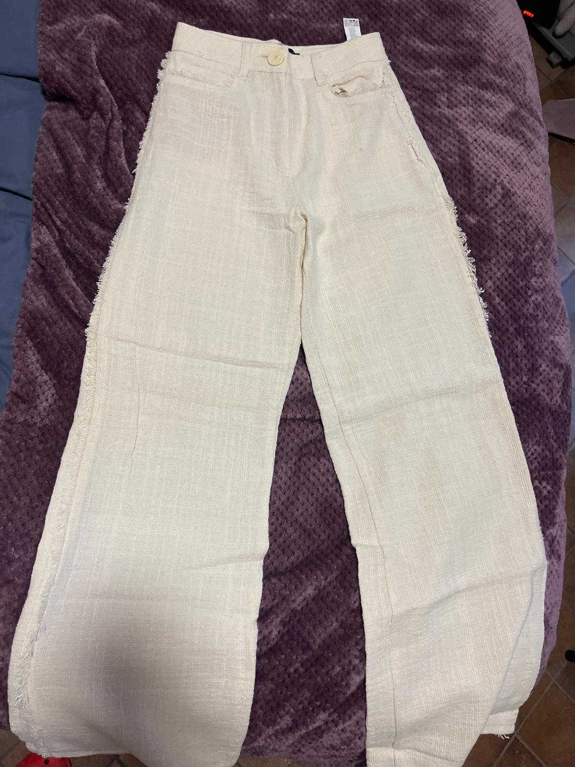 Beige textured fabric trousers with buttons, on a purple blanket. Partially visible background.