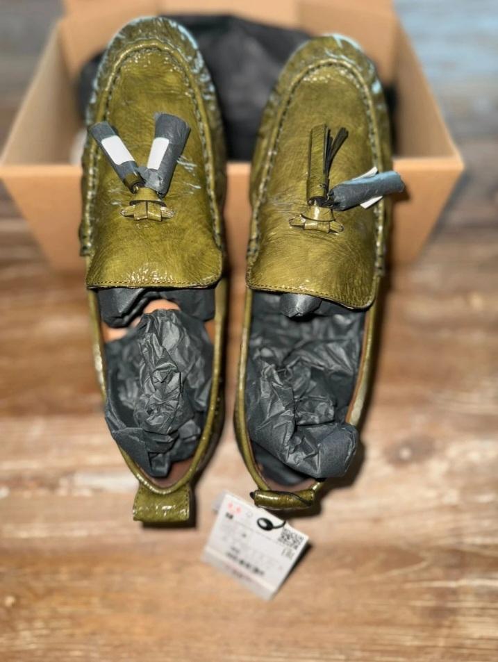 Green tassel loafers, stuffed with black paper, on a cardboard box. Label visible at the bottom.