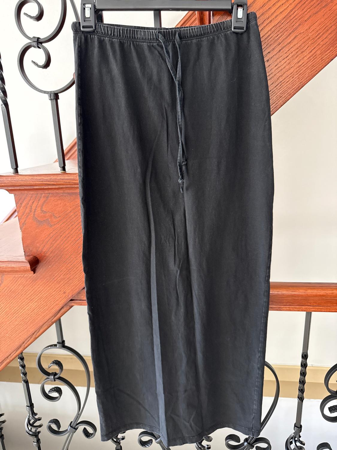 Black pants hanging on a hanger over a wood and wrought iron railing. Wooden staircase in the background.
