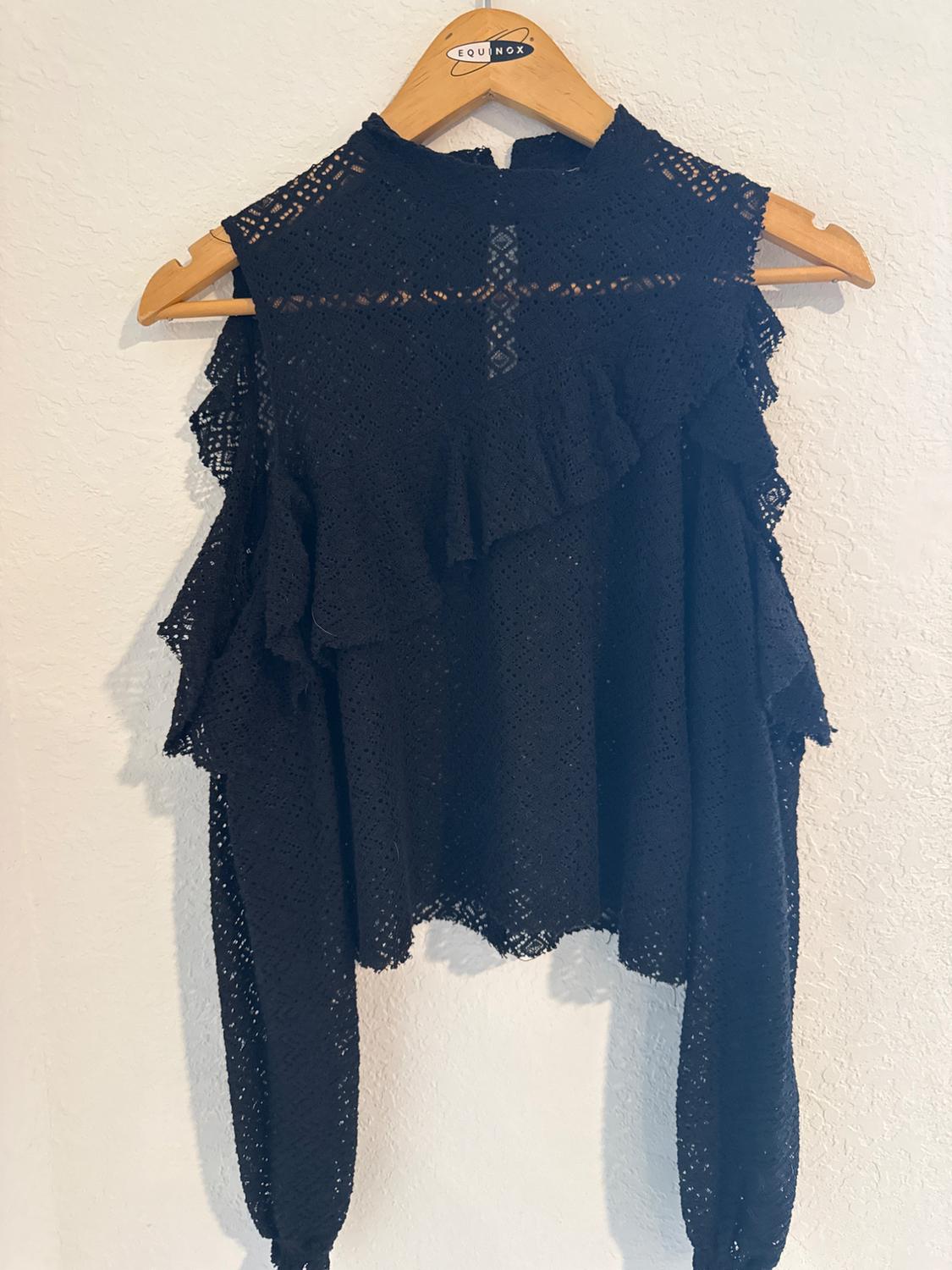 Black ruffled lace blouse, hanging on a wooden hanger with the "Equinox" brand visible, against a white wall.