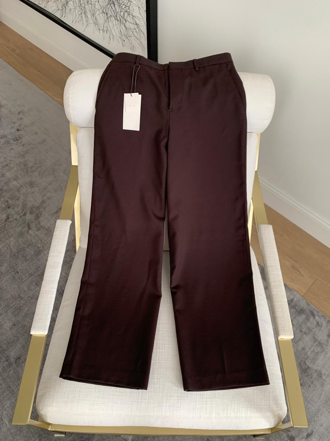 Dark brown trousers with a label, on a white chair with gold details in an indoor setting with a grey carpet.