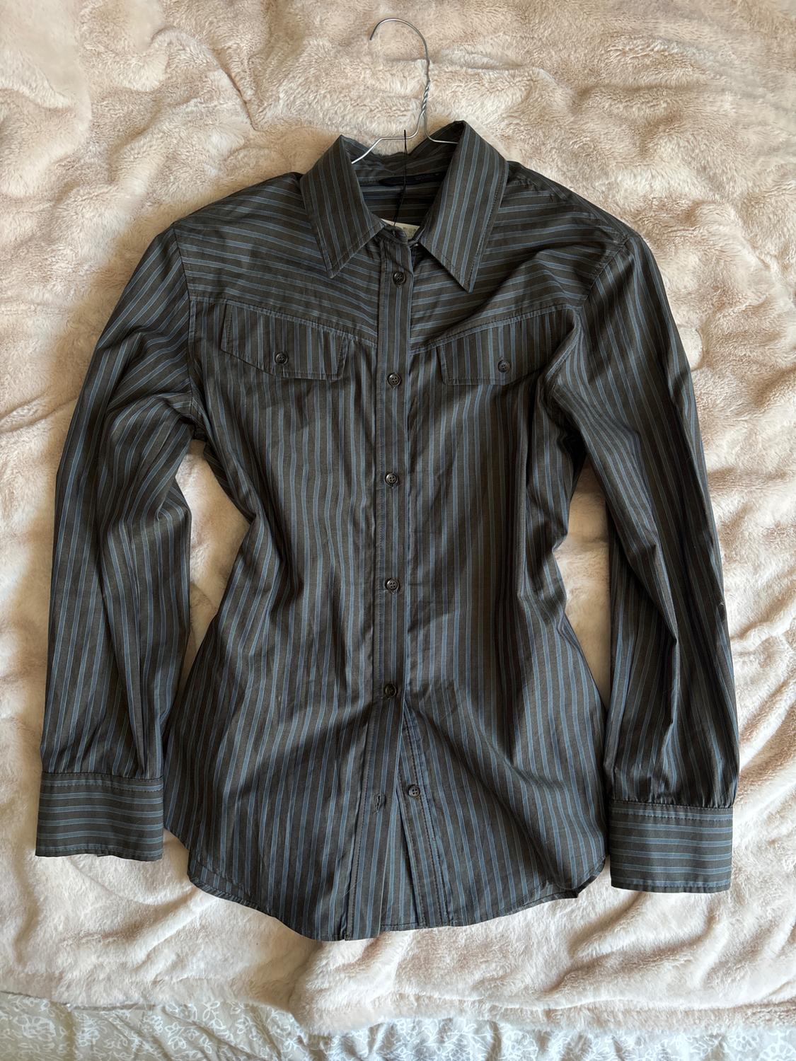 Dark grey shirt with blue stripes and chest pockets, on a wire hanger over a soft cream blanket.