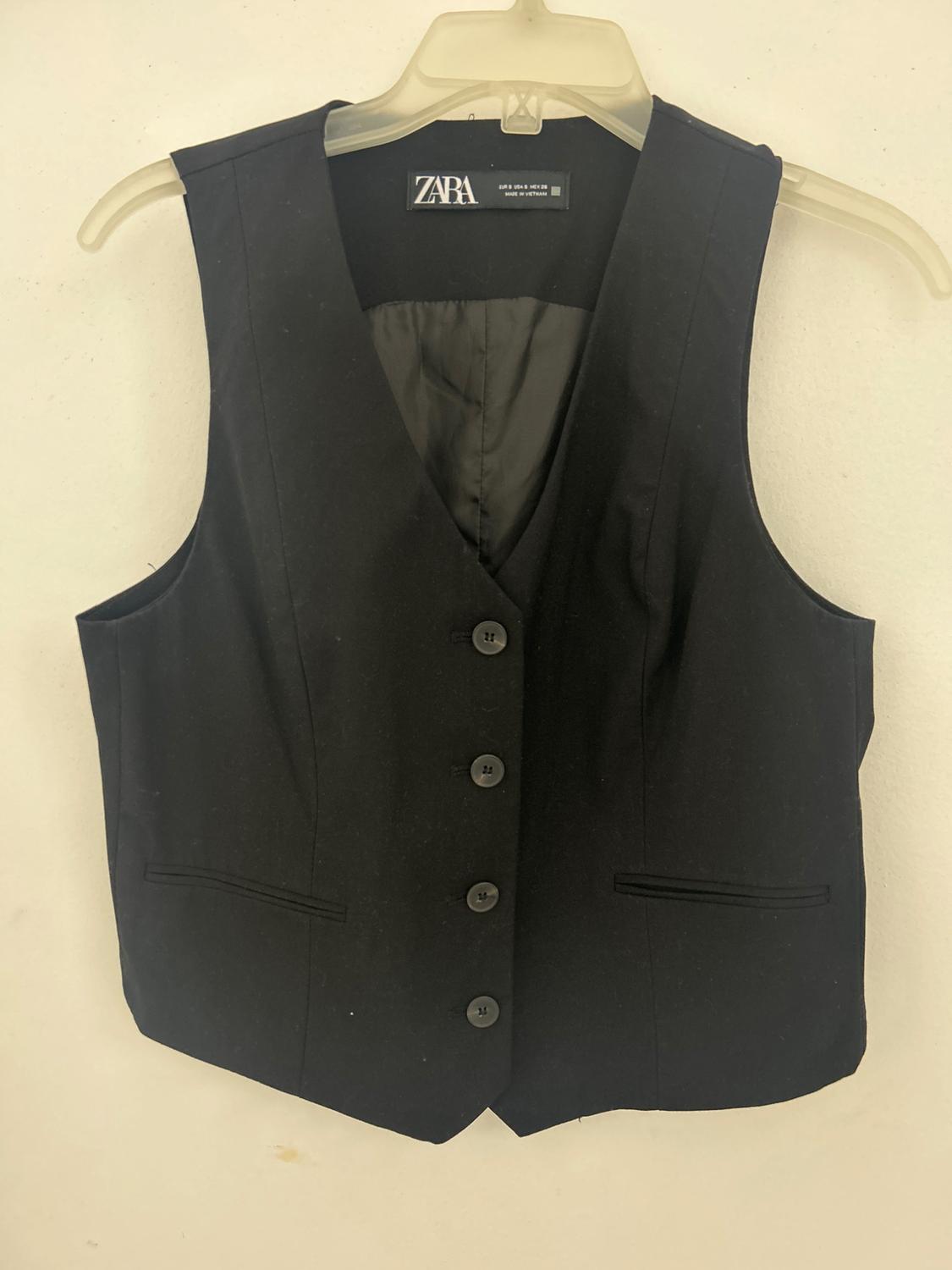 Black button-up vest hanging on a plastic hanger. Visible tag with the text "ZARA". White background.