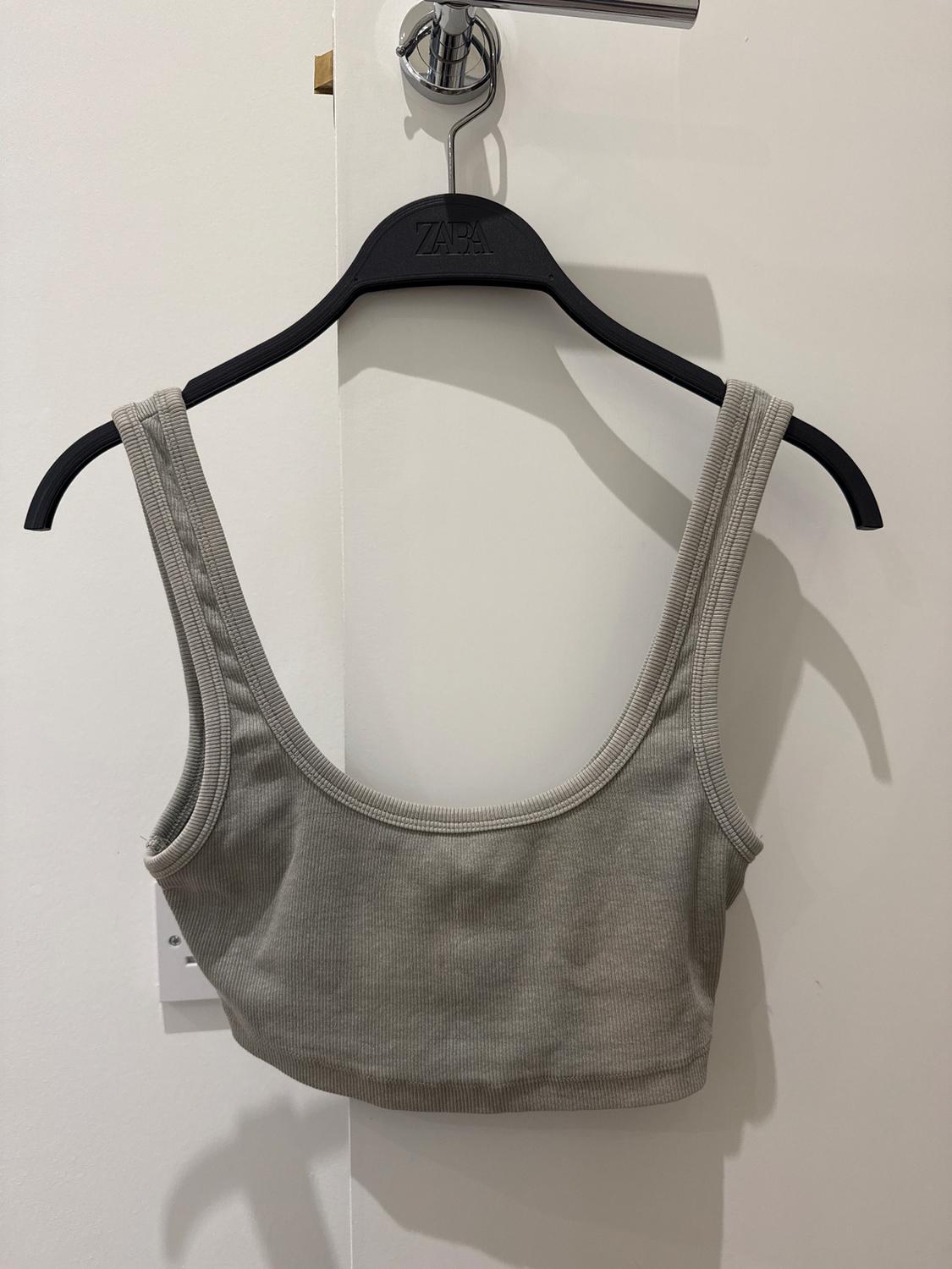 Grey sleeveless top hung on a black hanger with the brand visible, on a white background.