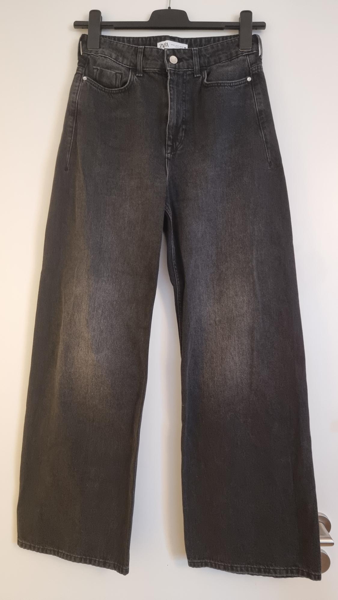 Baggy black denim jeans hanging on a black hanger against a white background. Visible label on the waist.