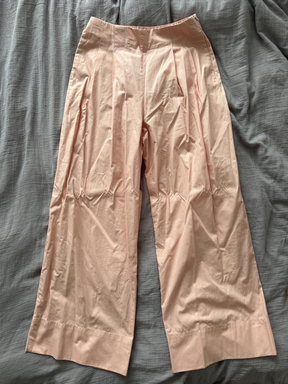 Light pink wide-leg trousers with pleats, placed on a wrinkled grey fabric.