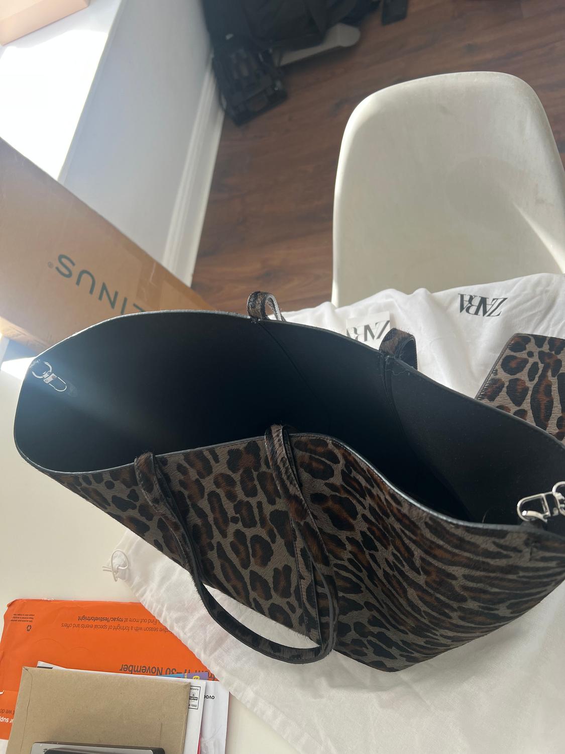 Animal print handbag on a white chair, next to a cardboard box and envelopes in a room with a wooden floor.