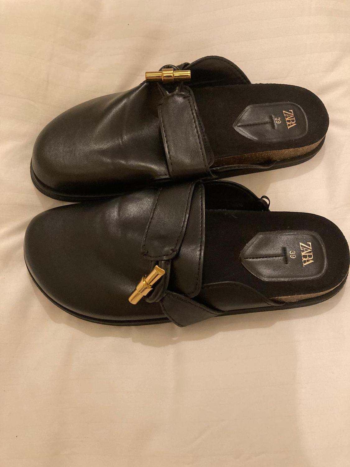 Black leather shoes with a gold detail on the upper, on a light surface. Insole with "ZARA" logo and size 39 visible.