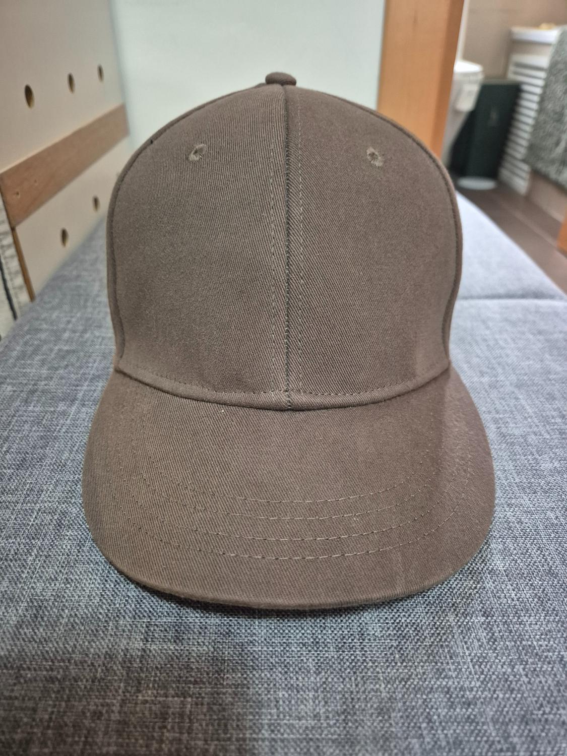 Brown cap on a grey surface, with a wooden background and white wall. Simple and casual design, front view.