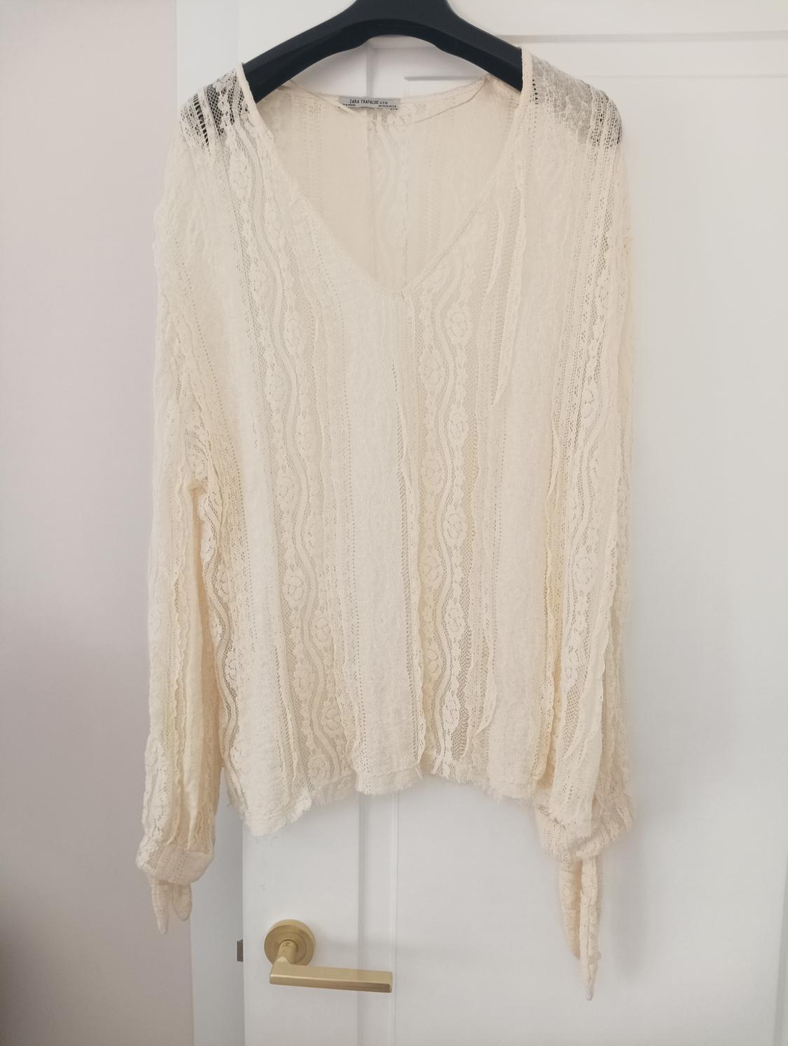 Beige lace blouse with a V-neck, hanging on a black hanger over a white door.