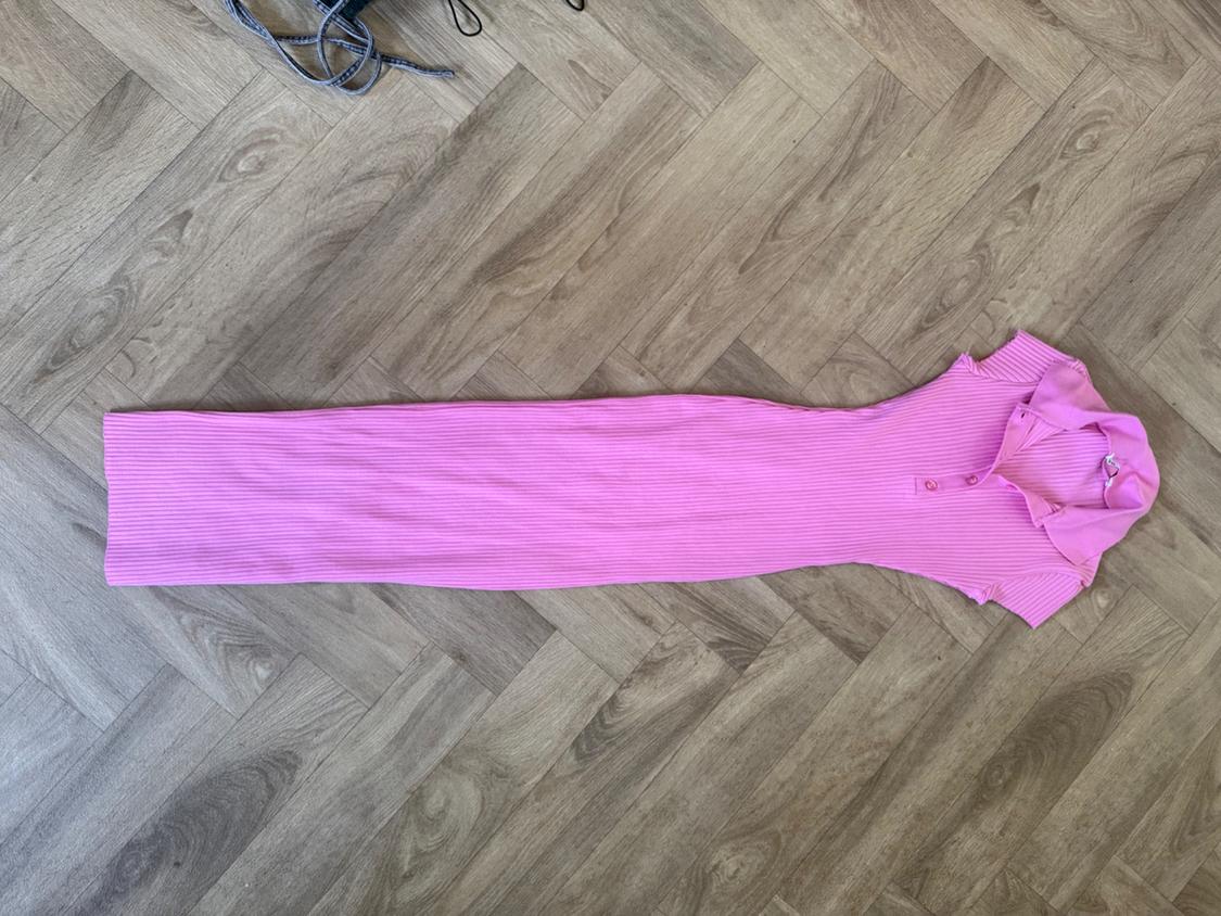 Pink ribbed maxi dress with a polo neck and short sleeves, laid out on a herringbone wooden floor.