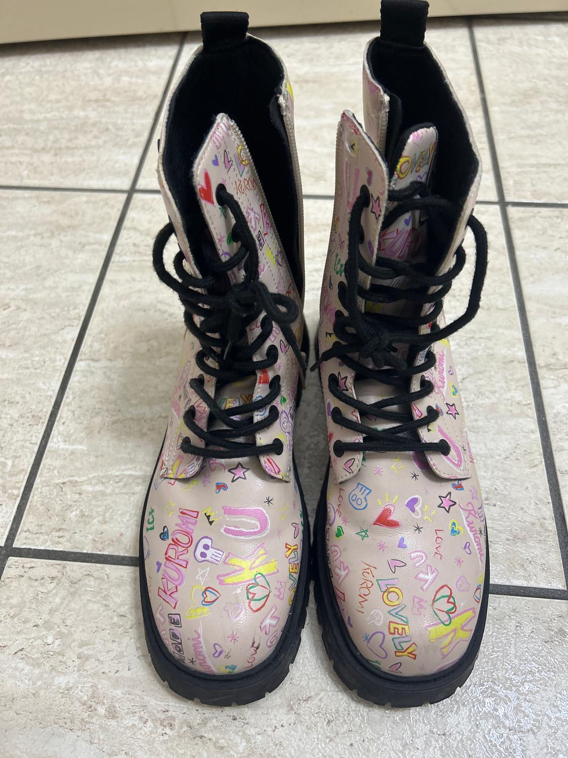 Pink boots with black laces, decorated with colourful drawings and words like "LOVE" and "KURAMI" on a light tiled floor.