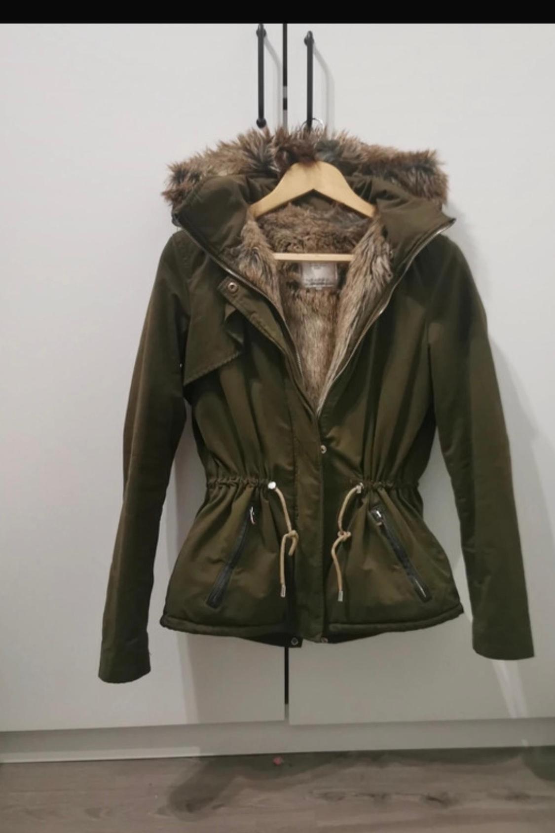 Front view of green jacket with fur hood, adjustable drawstrings and zipped side pockets.