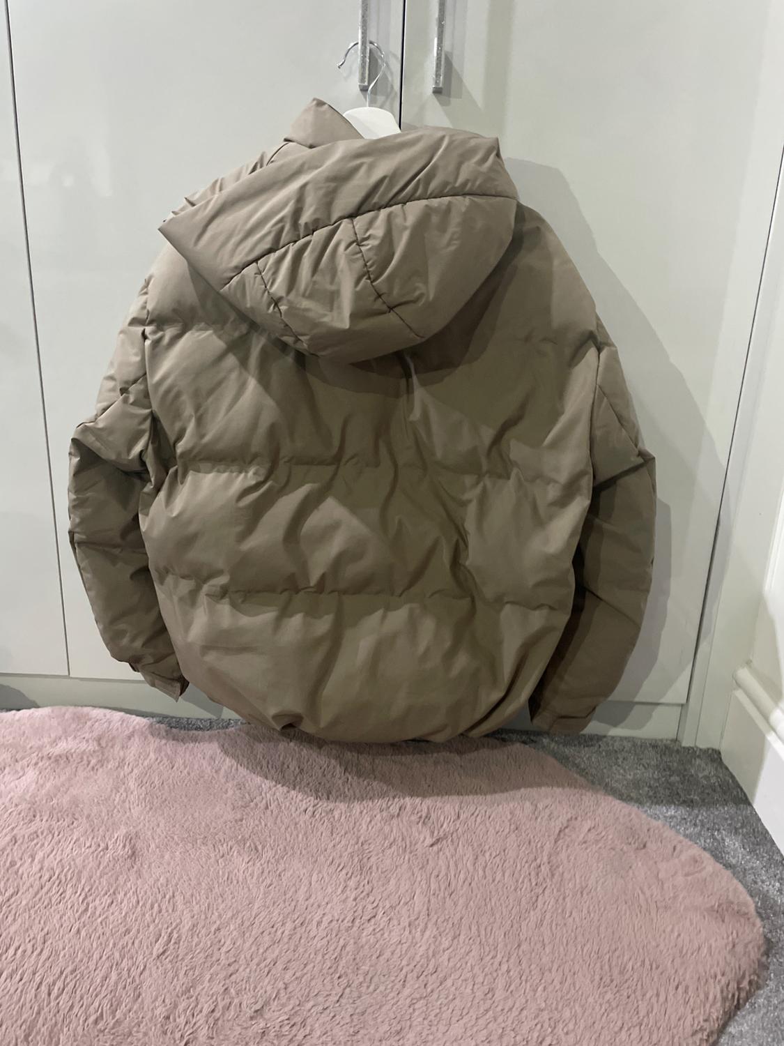Brown padded jacket hanging on a hanger in front of a white wardrobe, over a pink rug.
