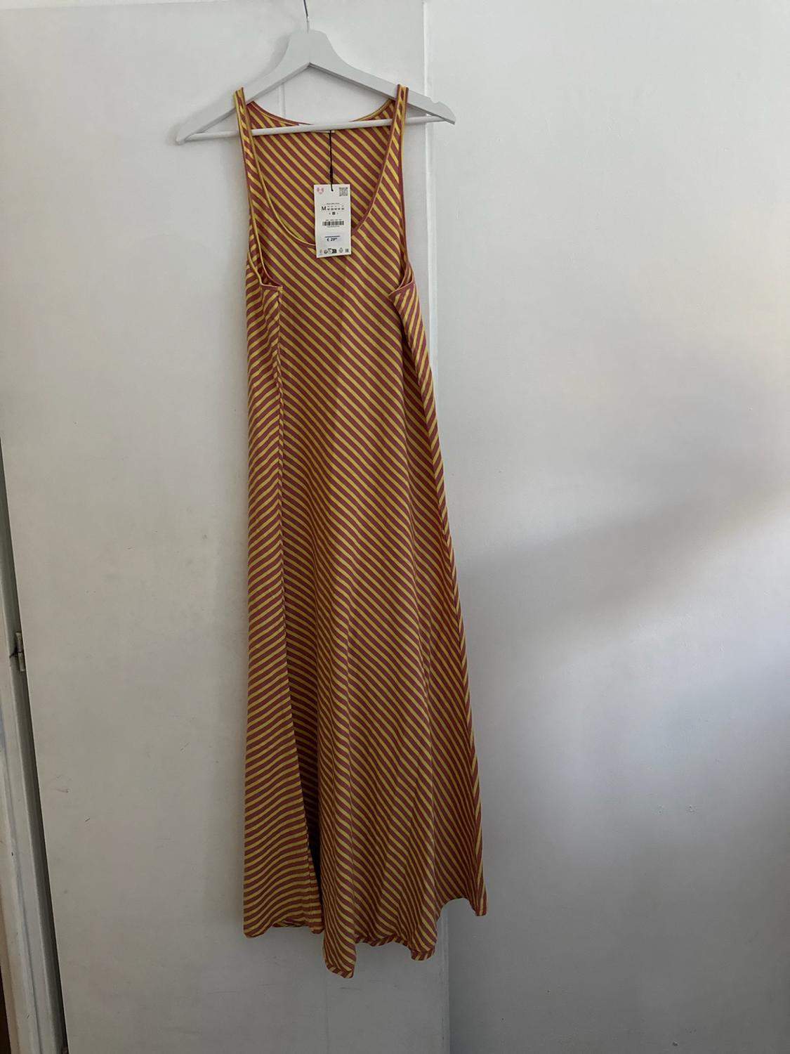 Long strappy dress with yellow and maroon diagonal stripes, hanging on a hanger on a white door. Relaxed style.