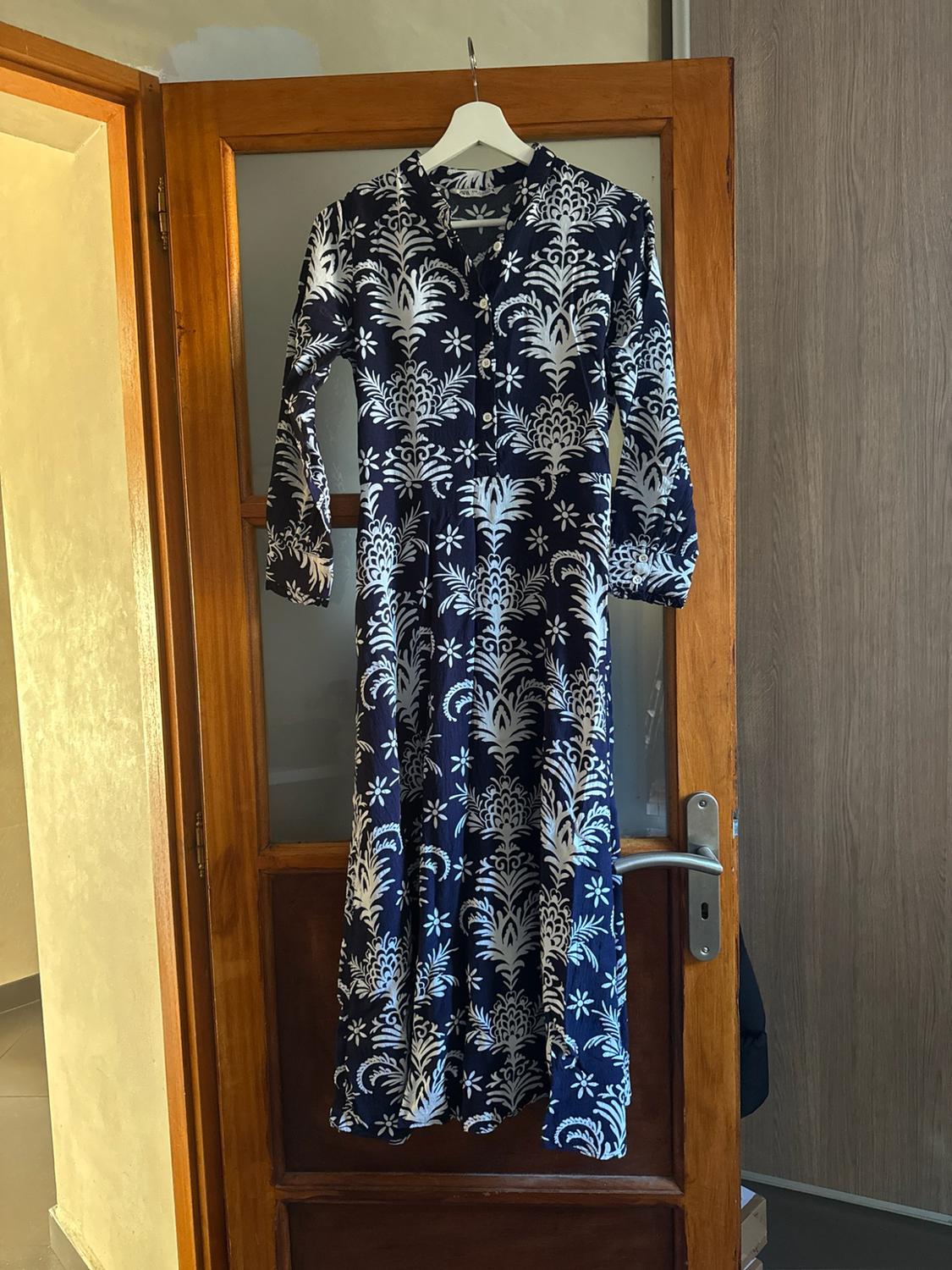 Navy blue maxi dress with a white print, hanging on a hanger on a wooden door with glass panels.