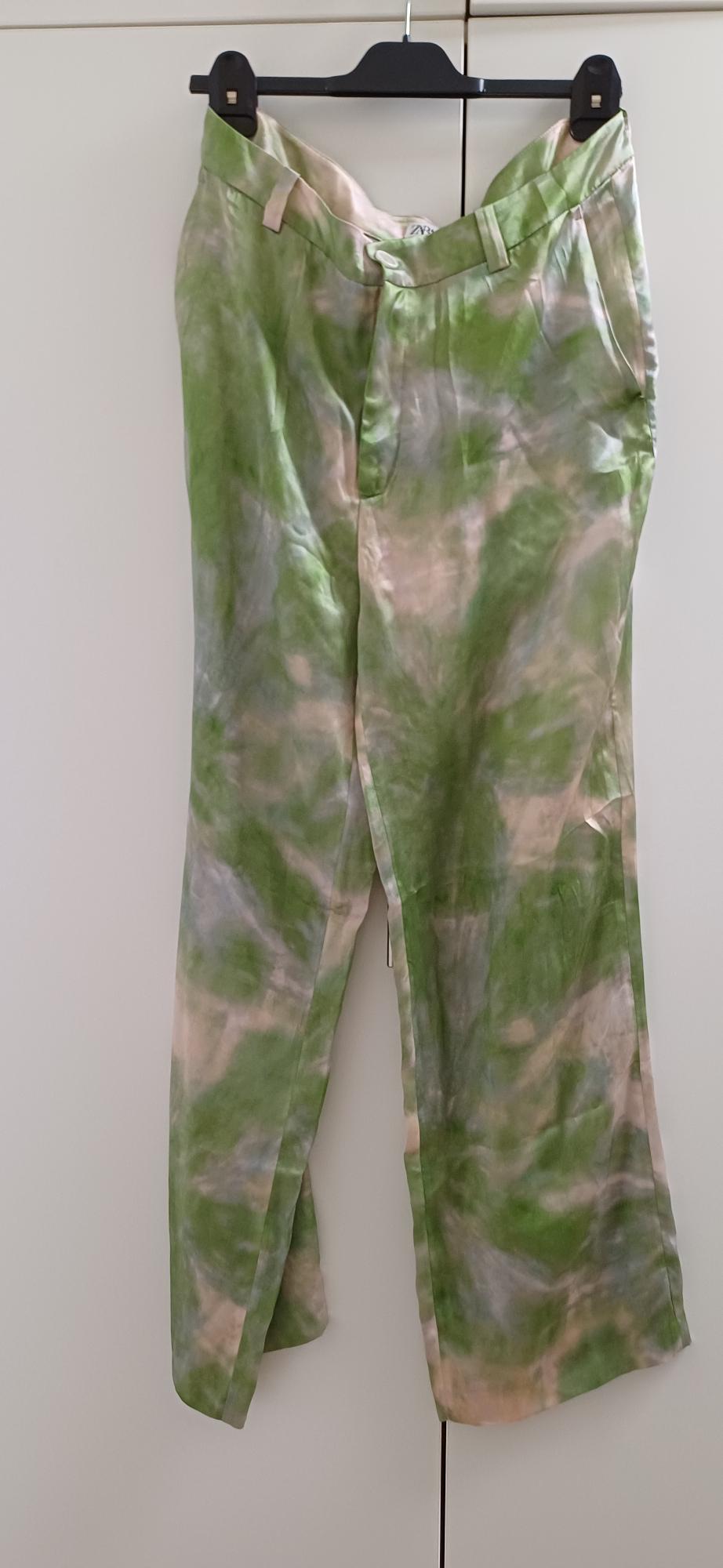 Trousers hanging on a hanger, with a tie-dye design in green and beige tones, on a white background.