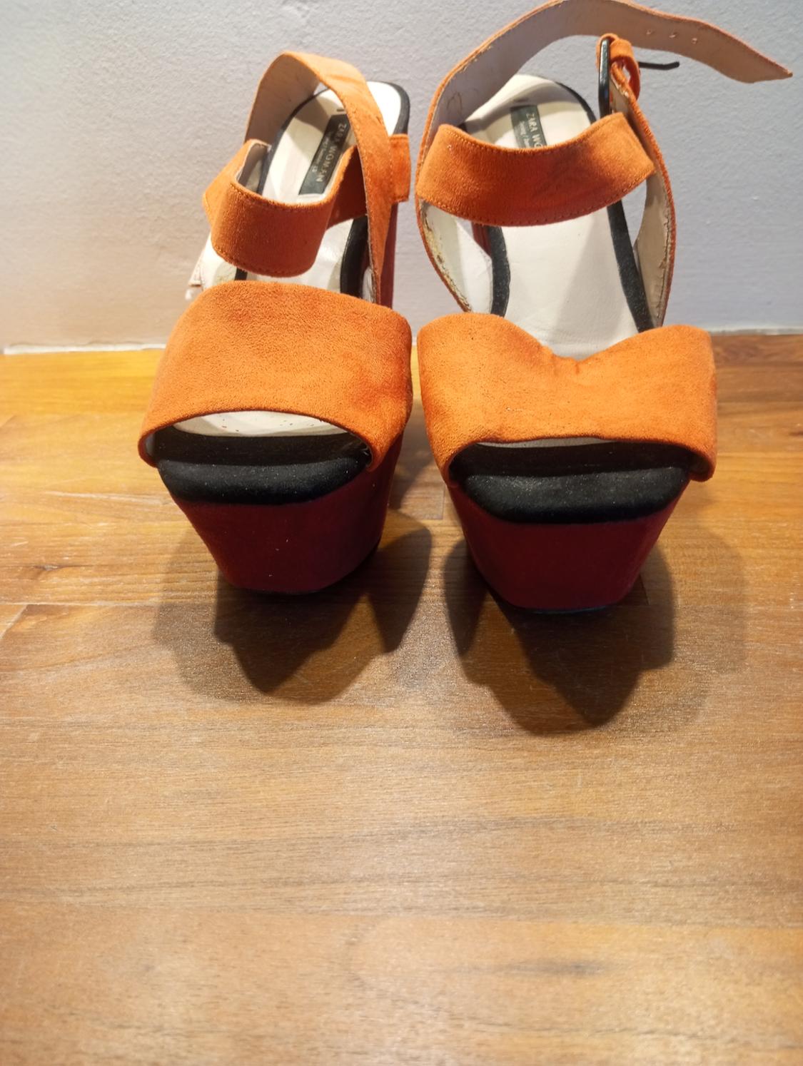 Orange high-heeled sandals on a wooden surface. Design with wide straps and a buckle fastening.