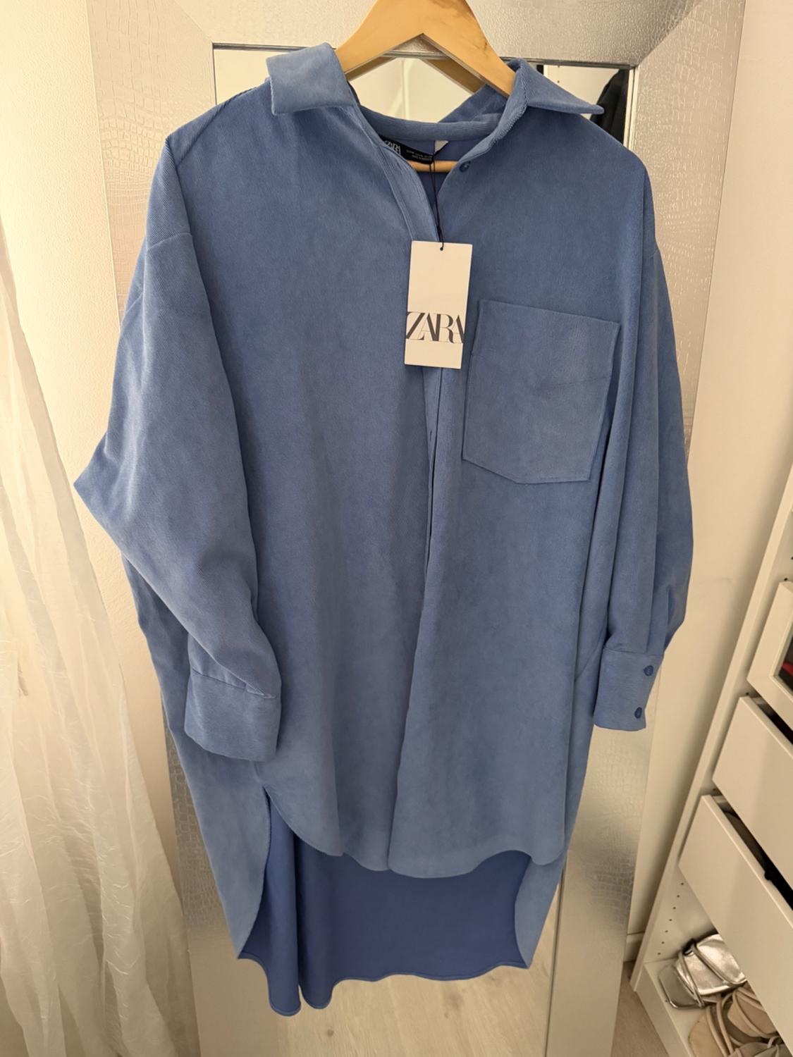Blue long-sleeved shirt hanging on a wooden hanger, with a visible "ZARA" tag, against a light background.