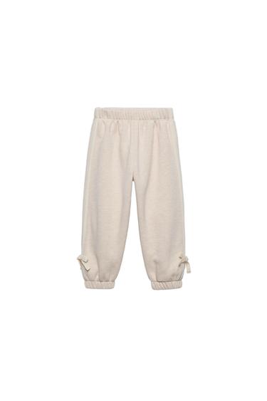 Front view of beige pants with elastic waistband and ankle ties.