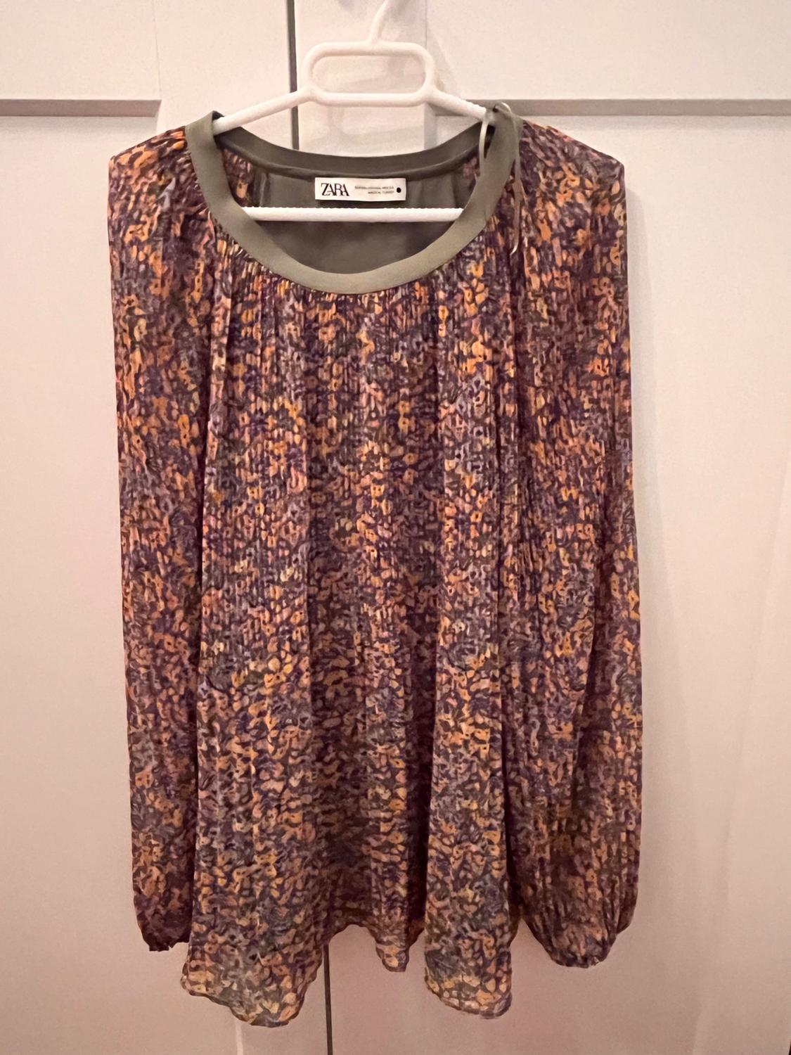 Long-sleeved blouse with a purple and orange abstract print, green collar. Hanging in a white wardrobe. ZARA label visible.